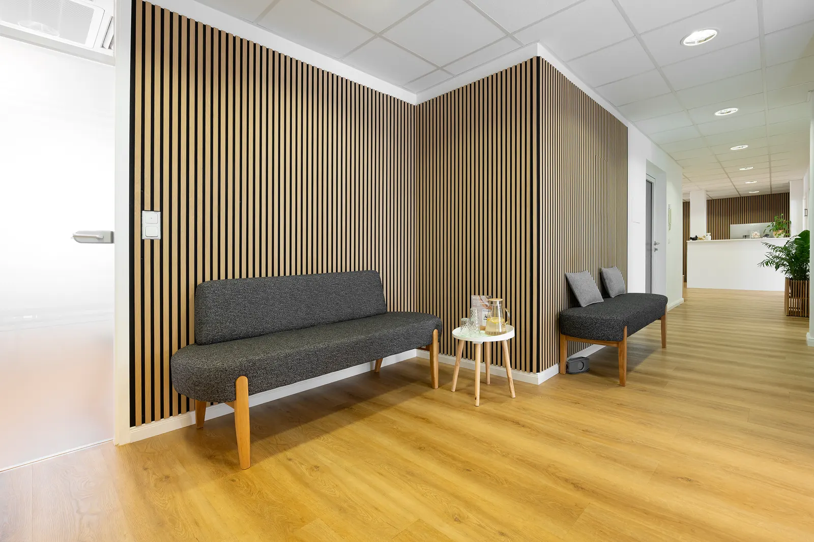 Waiting area with a grey sofa in front of a wooden slat wall